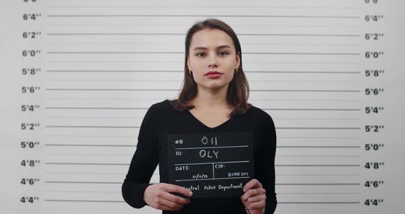 Mugshot of Young Attractive Woman with Holding Sign for Photo in Police Department alt