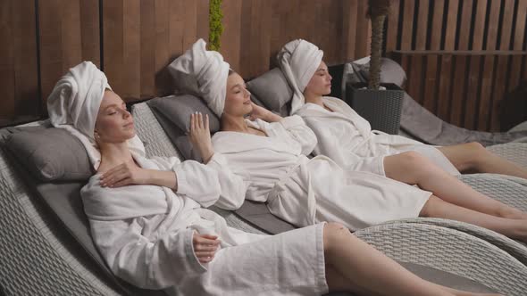 Calm Caucasian Women in Bathrobe and Towels Lying on Bed in Spa Center Having Rest Enjoying Time