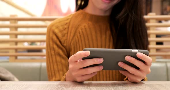 Woman Playing Game on Cellphone in Restaurant alt