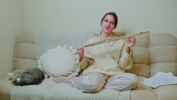 Woman musician with flute looking at video camera at home on sofa in living room
