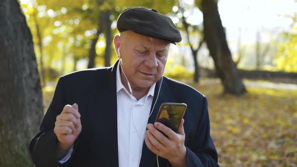 Joyful Man Having Fun When Talking on Phone Camera Through Headphones Outside alt