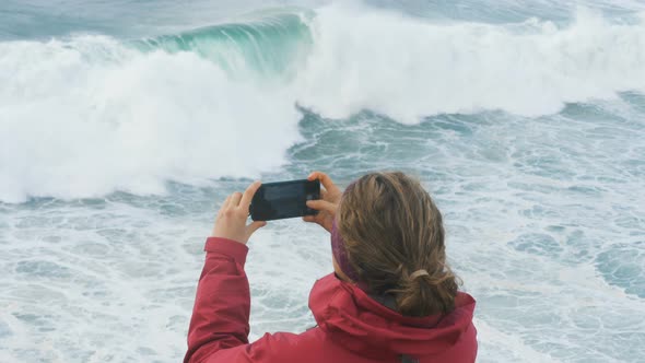 Girl in Jacket Takes Photos on Smartphone of Giant Ocean Waves Slow Motion alt
