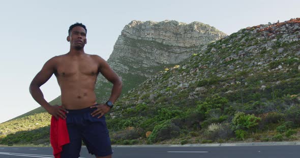 African american man standing and flexing his muscles on a coastal road alt