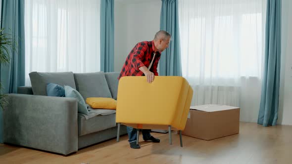 A Man in Home Clothes Assembles a Soft Chair Himself alt