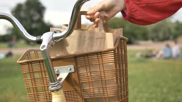 Woman Takes Out a Paper Bag of Food From a Vintage Basket on a Bicycle in a Park, Takeaway Delivery alt