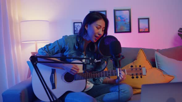 Happy asia girl blogger play guitar and use microphone sing song record music sound mixer on laptop.