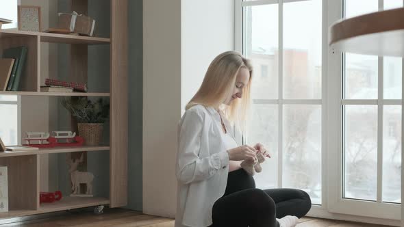 pregnant woman at the window walks on her stomach with baby socks