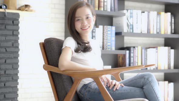Beautiful portrait young asian woman sitting on chair with smile and happy at living room. alt
