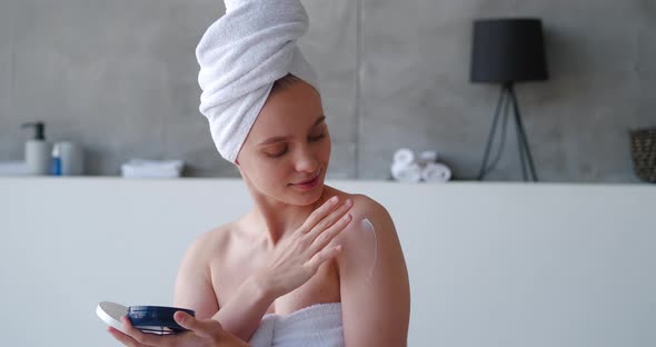 Closeup of a Pretty Woman Wrapped in White Bath Towel in Bathroom Opening a Container with Beauty alt