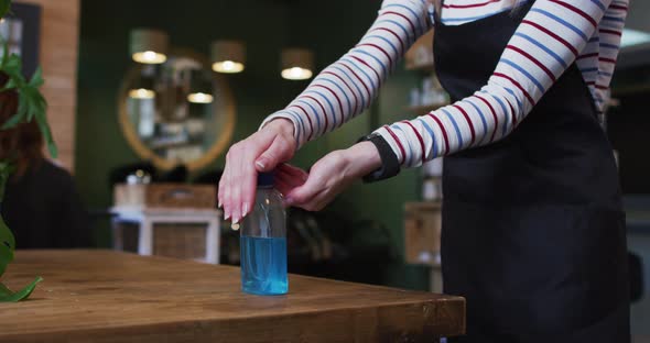 Mid section of female hairdresser sanitizing her hands at hair salon alt