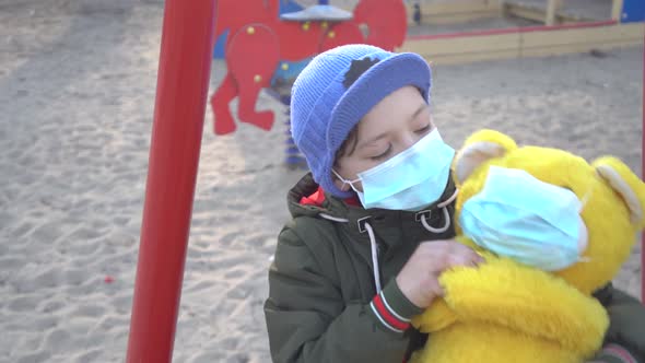 Portrait of Cute Boy in Face Mask Hugging Yellow Teddy Bear and Looking at Camera alt