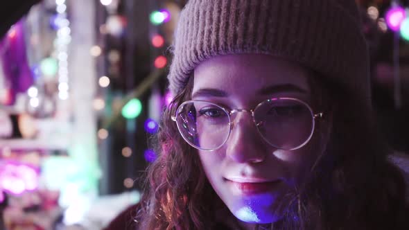Curly Girl with Christmas Lights. Young Woman in Glasses and a Winter Knitted Hat. The Cute alt