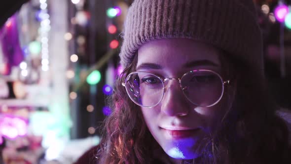 Curly Girl with Christmas Lights. Young Woman in Glasses and a Winter Knitted Hat. The Cute
