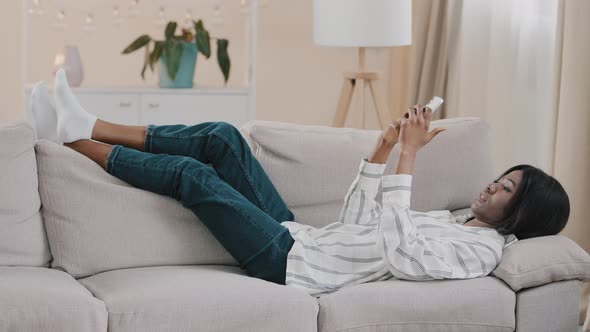 Relaxed Carefree Young Calm Woman Lying on Comfortable Couch in Cozy Living Room Typing Message on alt