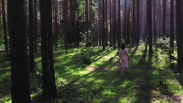 A Girl in a White Dress Walks Through the Woods