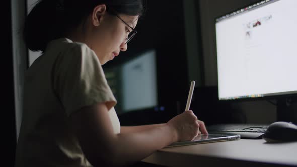 A young woman writes an article on a tablet at night in a home office.