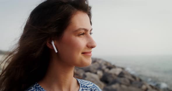 Beautiful Woman with Wireless Headphones in Her Ears Smiling Looking at the Sea alt