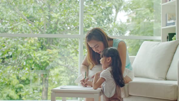 Young mother teaching cute daughter drawing on paper
