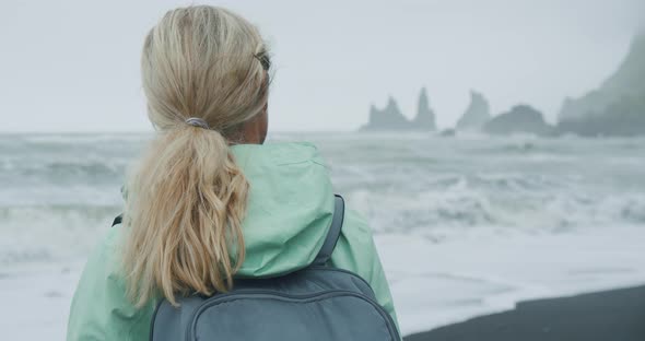 Woman with a Green Raincoat Walking on a Black Sand Beach Enjoying View to Reynisfjara Sea Stack alt