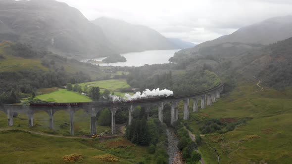 Steam train crossing Glenfinnan viaduct in Scotland on a rainy day