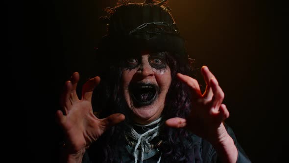 Sinister Senior Mature Woman in Carnival Costume of Halloween Witch Making Faces Trying to Scare alt