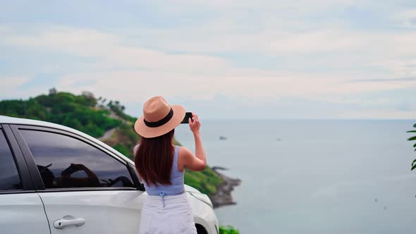 Young woman traveler taking a photo at the beautiful sea view with her car