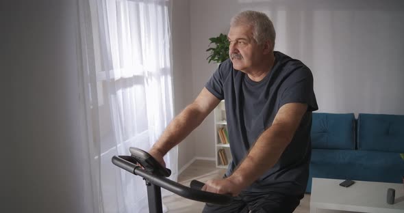 Middle Aged Man Is Training at Home Spinning Pedals of Exercise Bicycle in Living Room Healthy alt