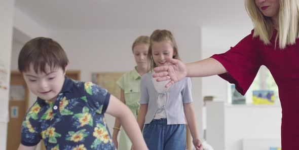 Small Nursery School Children with Female Teacher on Floor Indoors in Classroom Doing Exercise alt