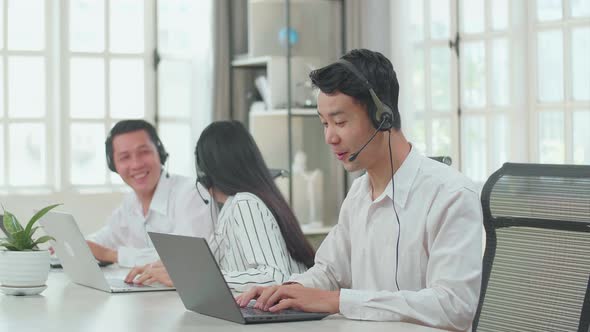 A Man Of Three Asian Call Centre Speaking To Customers While His Colleagues Talking With Each Other alt