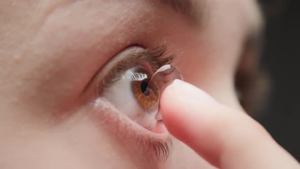 Closeup of a Browneyed Young Woman Putting on the Contact Lens with Fingers and Blinking alt