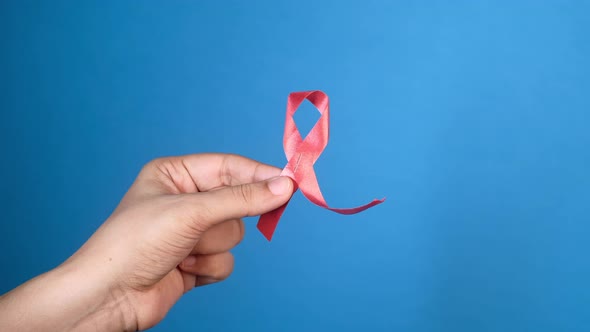 Hand Holding Red HIV Ribbon with Copy Space on Blue Background  alt
