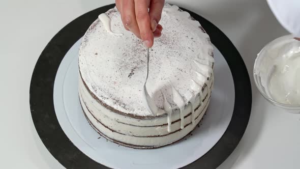 Top View of a Baker Pouring Melted White Chocolate on the Edges of the Cake so It Drips Down the