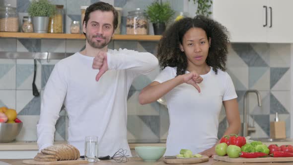 Mixed Race Couple Showing Thumbs Down Sign in Kitchen alt