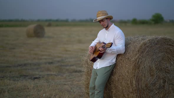 Man Wearing a Straw Hat Playing the Guitar About a Haystack