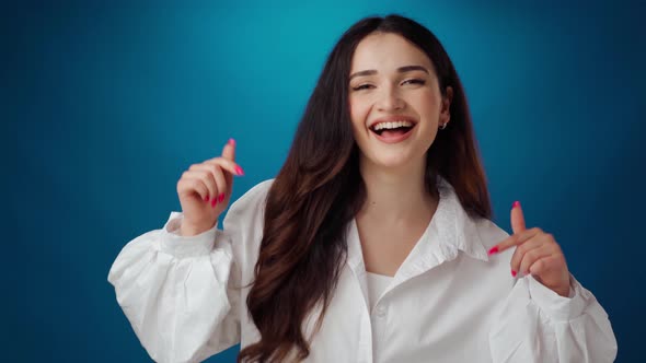 Smiling Brunette Woman Pointing Down Showing Advertising Against Blue Background