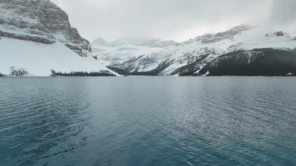 Aerial footage of the surface of Bow Lake with snow-capped mountains in Alberta, Canada alt