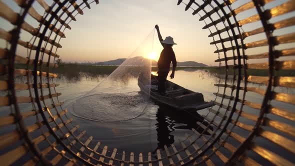 Silhouette fisherman throwing fishing net during sunset with boats at the lake.