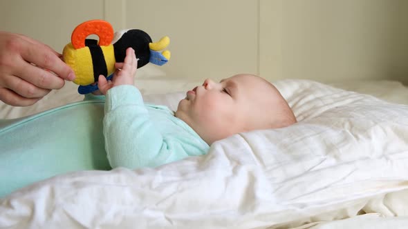 Cute Newborn Baby Lying on the Back and Plays with Toys alt