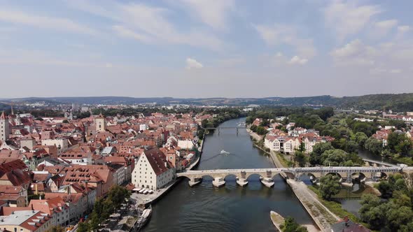 Aerial flyover above of Regensburg city, Historic Stone Bridge and Eiserner Steg cross Danube river alt