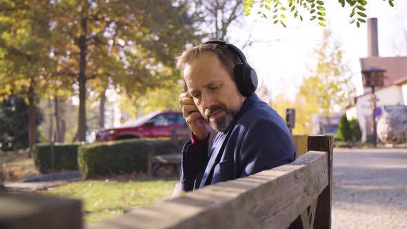 A Middleaged Handsome Caucasian Man Listens to Music with Headphones As He Sits on a Bench