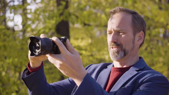 A Middleaged Handsome Caucasian Man Takes Pictures with a Camera in a Park in Fall