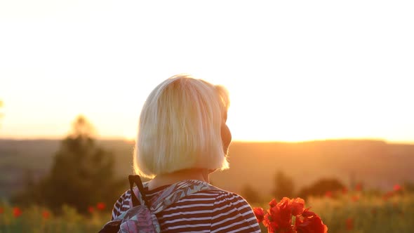 Adult Caucasian Woman Tourist with Backpack and Poppy Flower Bouquet at Sunset in the Field