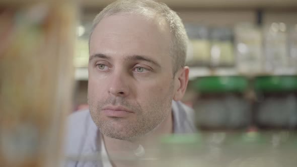 Close-up Face of Focused Confident Man Looking at Canned Food on Shelf. Portrait of Focused alt