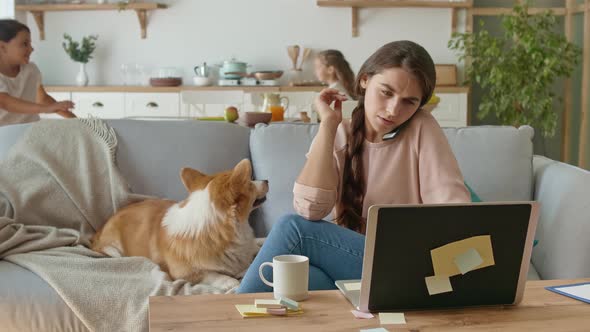 On The Background Daughters Are Running Around The Table, While Their Mother Working With a Laptop alt