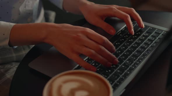 Woman Typing on a Laptop with a Cup of Coffee