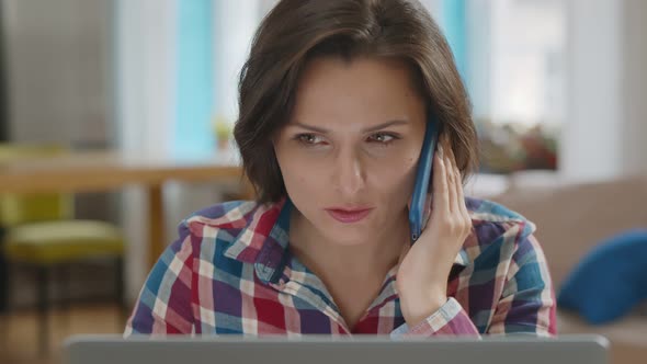 Young Woman Freelancer Working on Laptop Talking with Client on Phone at Home alt
