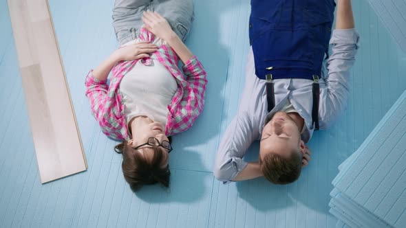 Man and Woman Lying on Expanded Polystyrene Floor Rejoicing at Job Done While Installing Laminate alt