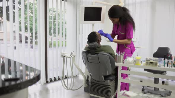 Pretty Young Female African Dentist Examining Her Handsome Male Dark Skinned Patient with alt