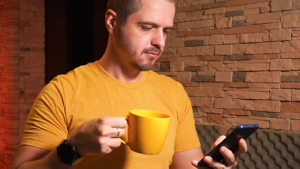 Man Texting or Browsing Online Using Smartphone and Drinking Tea or Coffee