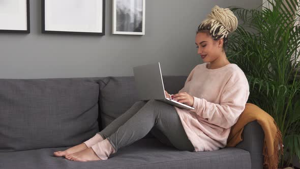 Young Attractive Woman Working on Laptop While Sitting on Modern Sofa at Home